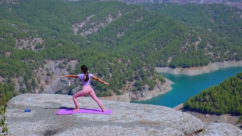 Woman Practicing Yoga on Rock Cliff with Panoramic Mountain and Lake View