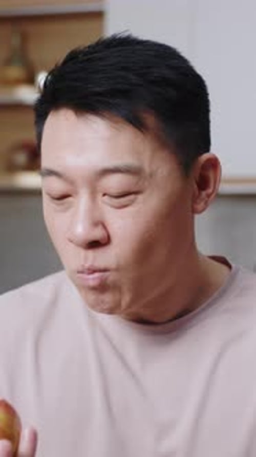 Cheerful Man Eating a Red Apple in Kitchen
