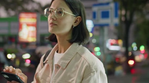 Young Woman Using Smartphone on City Street in Evening