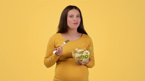 Pregnant Woman Eating Fruit Salad on Yellow Background