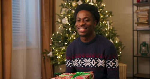 Man Smiling Holding Christmas Gift Near Christmas Tree