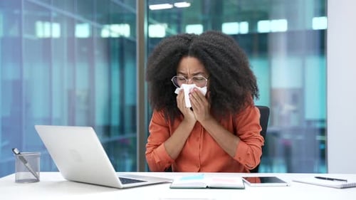 Sick young african american businesswoman suffering from seasonal allergies working on a laptop