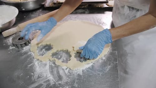 Process of Skillfully Preparing Cookies Cutting Dough on a Steel Table in a Bakery Setting