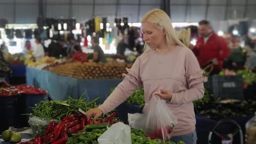 A Pretty Woman is Shopping at Market Picking Up Red Pepper in a Plastic Bag