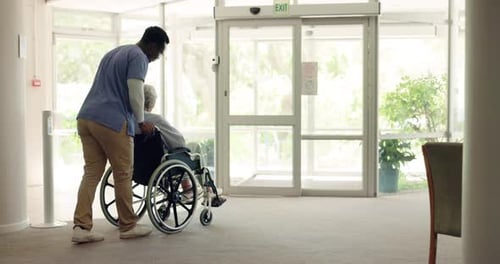 Caregiver Pushes Senior in Wheelchair Indoors