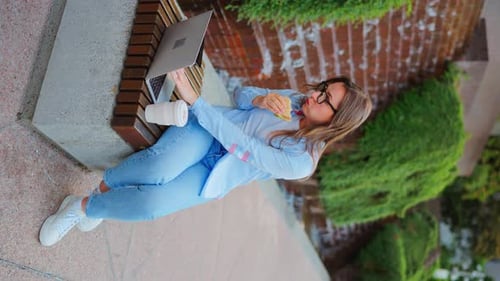 Frau beim Mittagessen mit einem Sandwich und Kaffee im Park mit einem Laptop