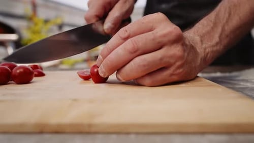 Man Slicing Cherry Tomatoes With Knife On Chopping Board