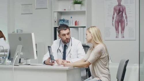Doctor Shows to His Woman Patient Tablet Computer with X-Ray Images on it. Doctor Point Out Detail