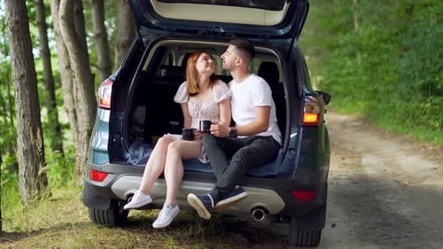 young couple Husband and wife on vacation sitting on a campsite in the car. Happy family on forest