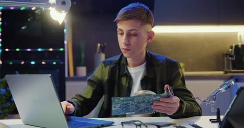 Atractivo adolescente moderno con gafas protectoras considerando la placa del ordenador en sus manos y leyendo