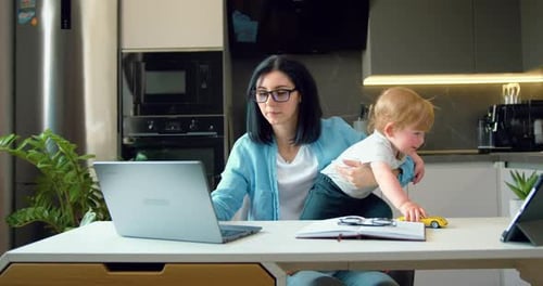 La mujer con su hijo pequeño se sienta en casa a la mesa y trabaja en el portátil. Estilo de vida independiente y madre