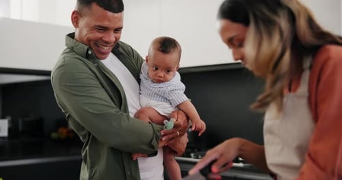 Man Holding Infant While Woman Cooks in Kitchen