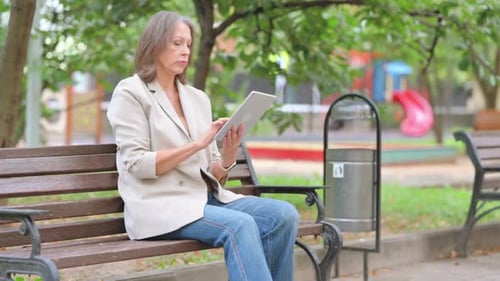 Old Woman Using Digital Tablet while Sitting Outdoor on Bench