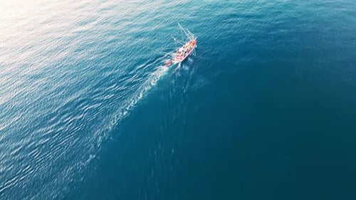 Luftdrohne überfliegt Fischersegelboot, sonnige Tageslichtreflektion auf blauem Wasser