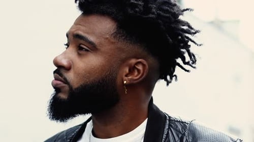 Close-up face of a pensive young black man walking forward in city street in tracking shot in