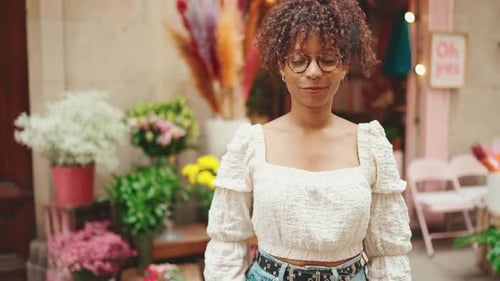 Woman in glasses stands next to a flower shop and looks at the camera smiling