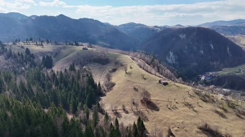 Sanfte Hügel und verstreute Bäume unter klarem Himmel, mit Bergketten im Hintergrund