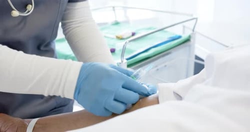 Diverse female doctor giving injection to senior female patient in hospital room, slow motion
