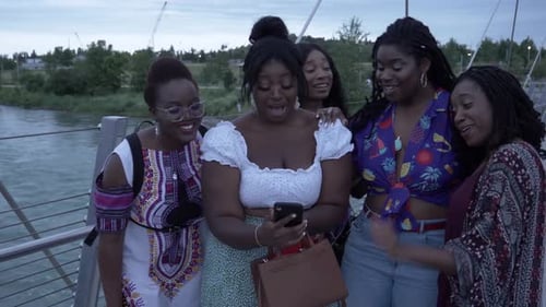 Happy stylish young women friends enjoying social media on an urban bridge