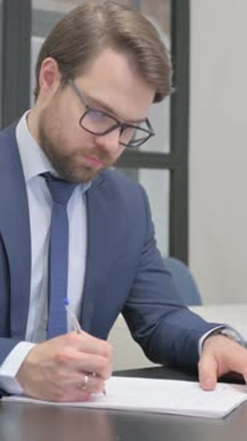 Man Writing on Paper at Desk in Office