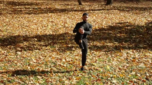 A Man Stretches His Leg Muscles in Autumn in a Park Covered with Leaves