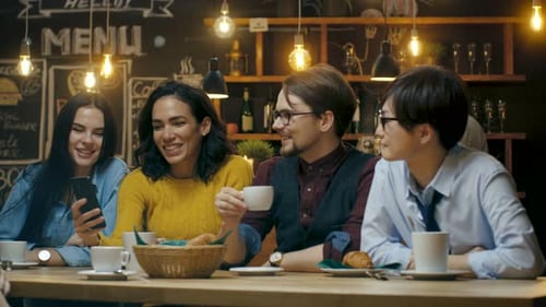 Friends Have Fun in Cafe, Drinking Hot Beverages, Talking and Using Smartphone. Beautiful Young Peo