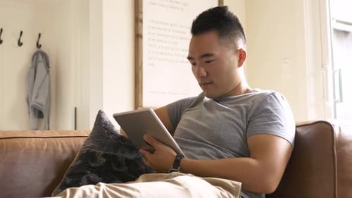 Man Relaxing On Sofa Using Tablet Device