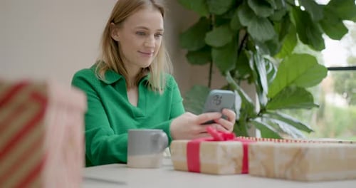 Female Buying Christmas Presents using Phone at Home and Wrapping Gifts