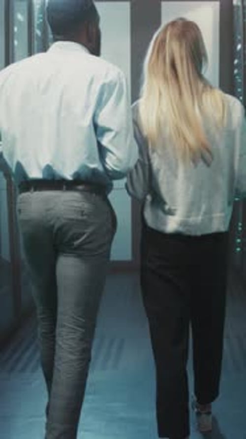 Employees Examine Network Hardware in Corridor Two Professionals Walk Through Data Center Inspecting