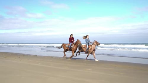 Two young women happily horseback riding along the beautiful beach coastline