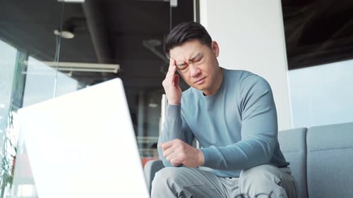 Young exhausted, overworked office worker sitting in the workplace with a severe headache massaging