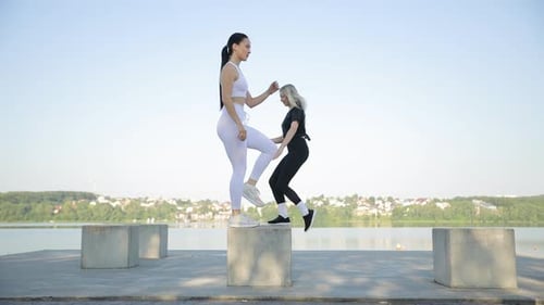 Fitness Training of Two Women Outdoors on the Background of the Lake