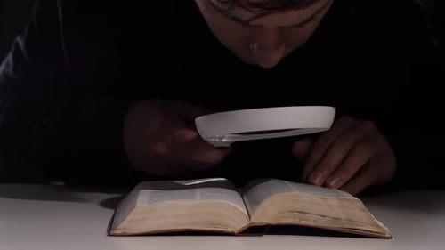 Forscher liest altes Buch mit Lupe in der Dunkelheit