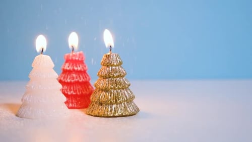 Snowing on Golden White and Red Christmas Tree Wax Candle Burning on Blue Background New Year or