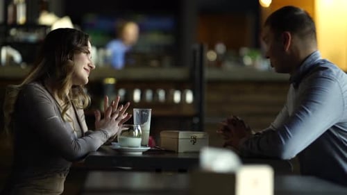 Side view of a young handsome man dressed in a shirt, talking to a woman in a cafe, sitting next to