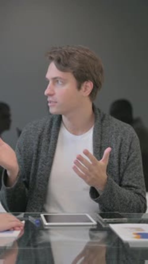 Man Sitting at Conference Table Talking and Gesturing