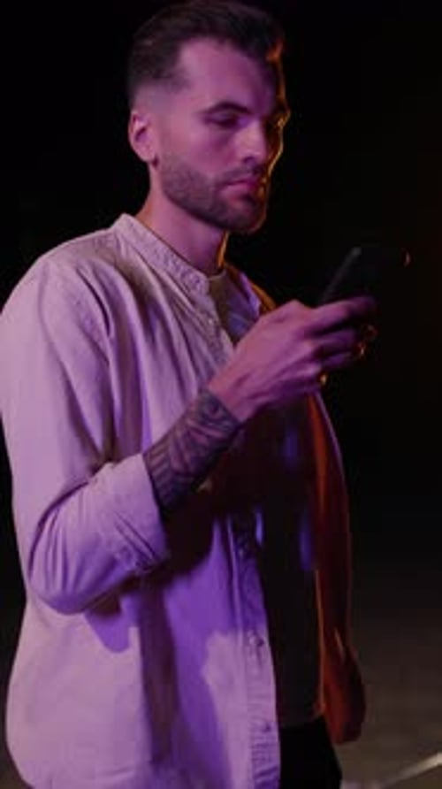 Vertical Footage of Young Focused Man in Casual Clothes Holding Smartphone in Hands in Evening