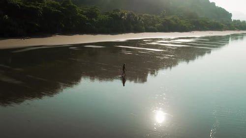Solo figure walking on glowing reflective Playa Hermosa beach during Costa Rica dawn