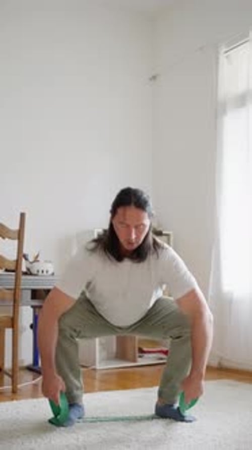 Man Does Squats With Resistance Band in Home