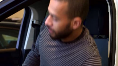 Young Man Enthusiastically Sits in a Car at the Dealership