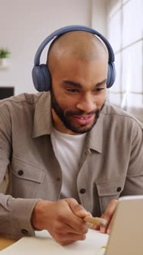 Man with Headphones Attends Online Meeting, Taking Notes