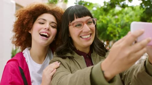 Playful female friends taking selfies with a phone outside in an urban park
