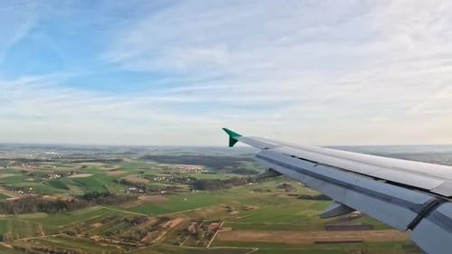 Aerial view of plane wing flying over rural farmland landscapes during flight descent