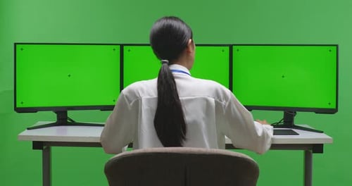 Back View Of Asian Woman Working With Mock Up Multiple Computer Monitor In Green Screen Studio