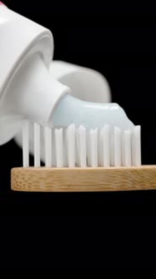 Vertical video. Toothpaste Is Applied to a Wooden Toothbrush, Close-up Isolated on Black Background.