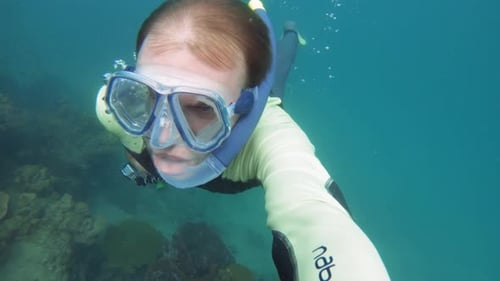 Male diver surfaces from underwater with bubbles surrounding him.