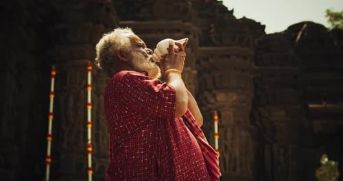 Photo authentique d'un moine indien âgé soufflant une conque dans un ancien temple en pierre. Personnes âgées