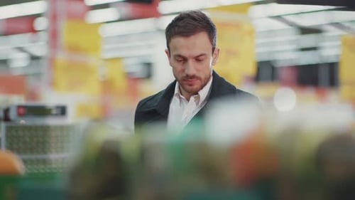 Young Man Walking in Supermarket with Shopping Trolley Which Looking on Shopping List in Phone Light