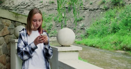Happy Smiling Teen Girl Reading Message in Phone Walking in Nature Park