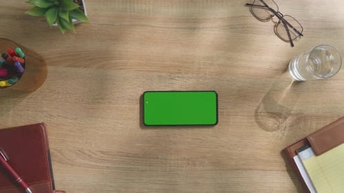 Top down view of a mock up green screen smartphone on a wooden desk